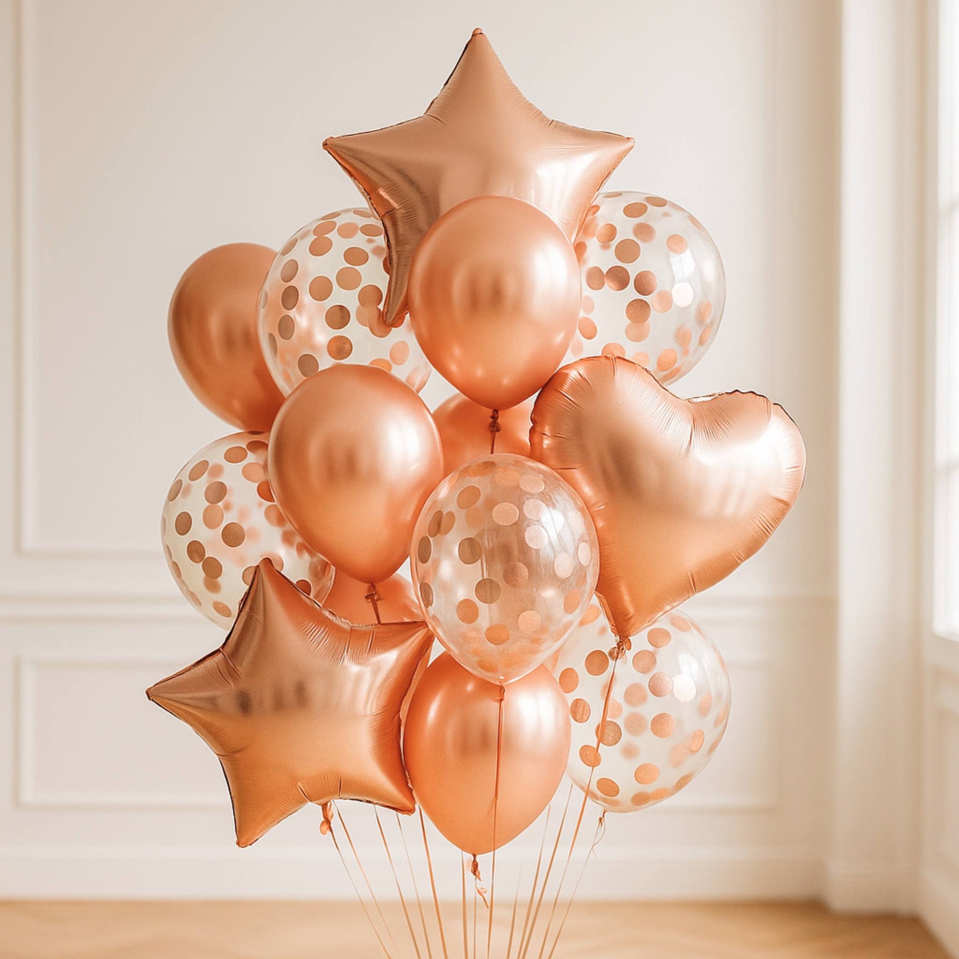 Rose gold balloons with star and heart shapes against a white wall.