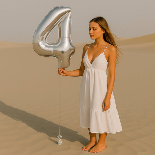 Woman in a white dress holding a large silver number '4' balloon in a desert setting