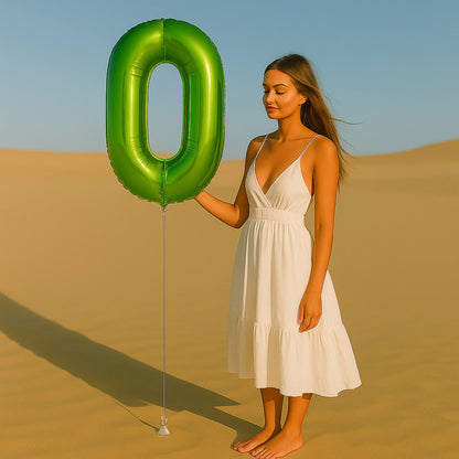 Woman in a white dress holding a large green number zero balloon in a desert setting