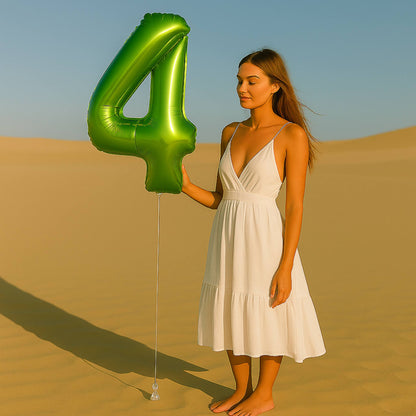 Woman in a white dress holding a large green number '4' balloon in a desert setting