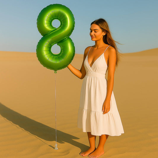 Woman in a white dress holding a large green number 8 balloon in a desert setting