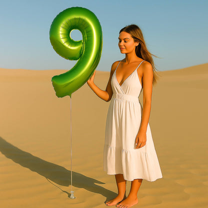 Woman in a white dress holding a large green number 9 balloon in a desert setting
