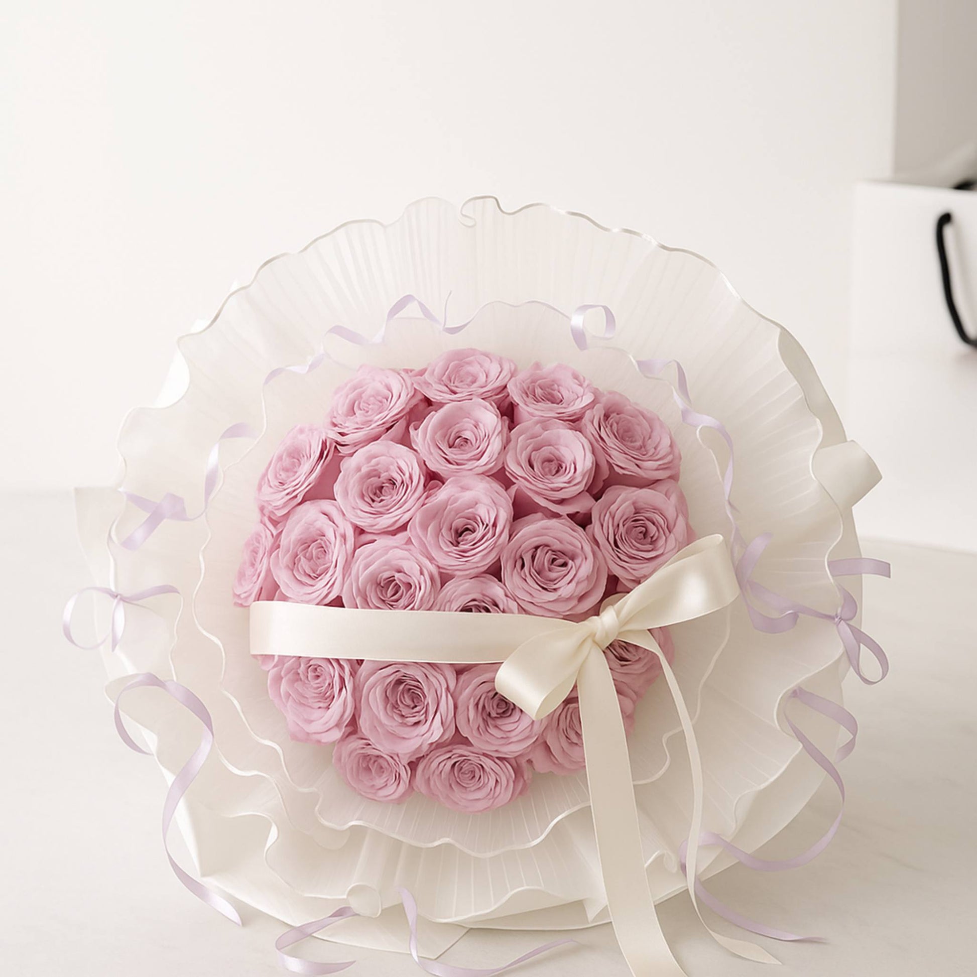 Bouquet of pink roses wrapped in white paper with a bow on a light background