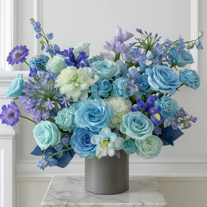 Bouquet of blue, purple, and white flowers in a gray vase on a marble surface.