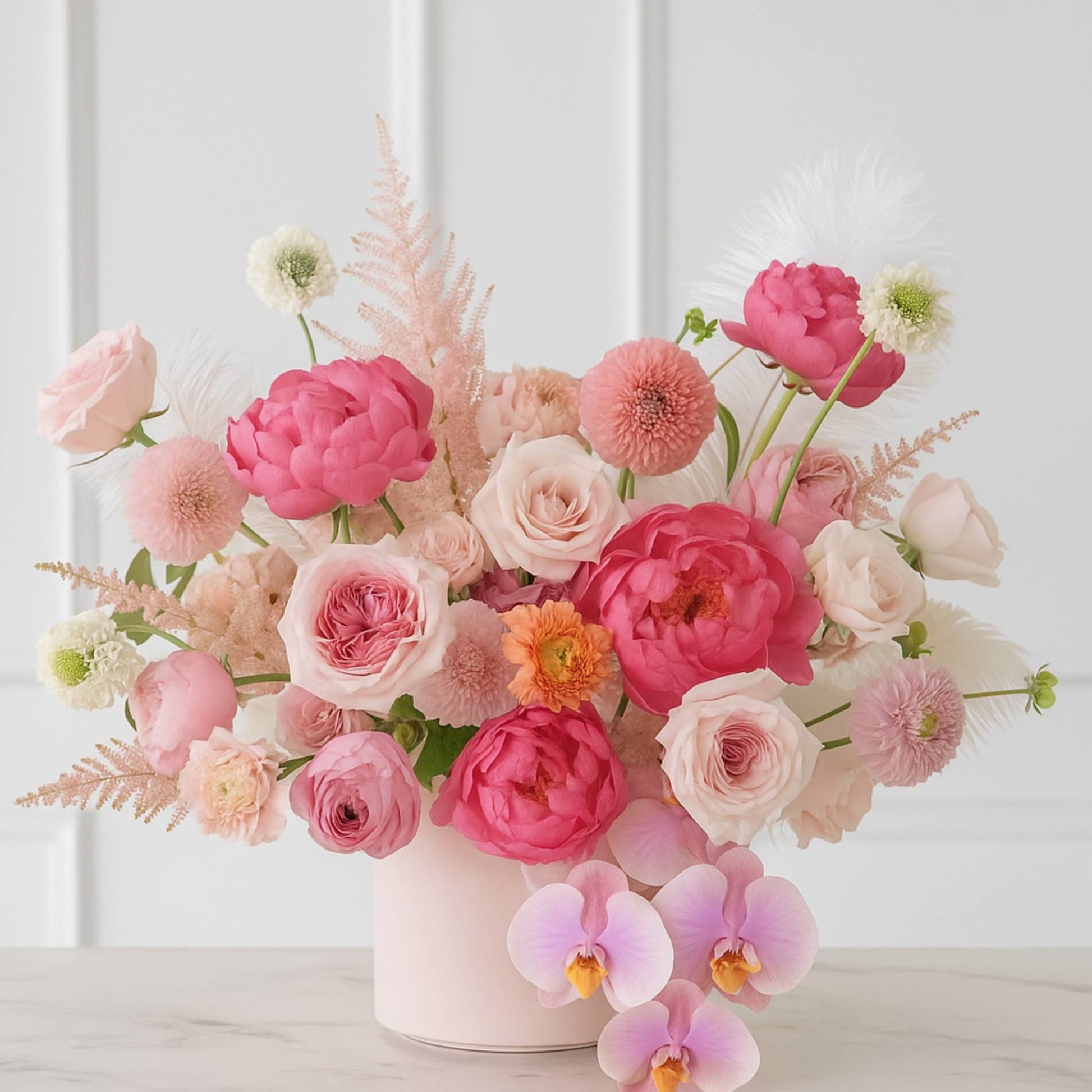 Bouquet of pink and white flowers in a vase on a light wooden surface with a white paneled background.