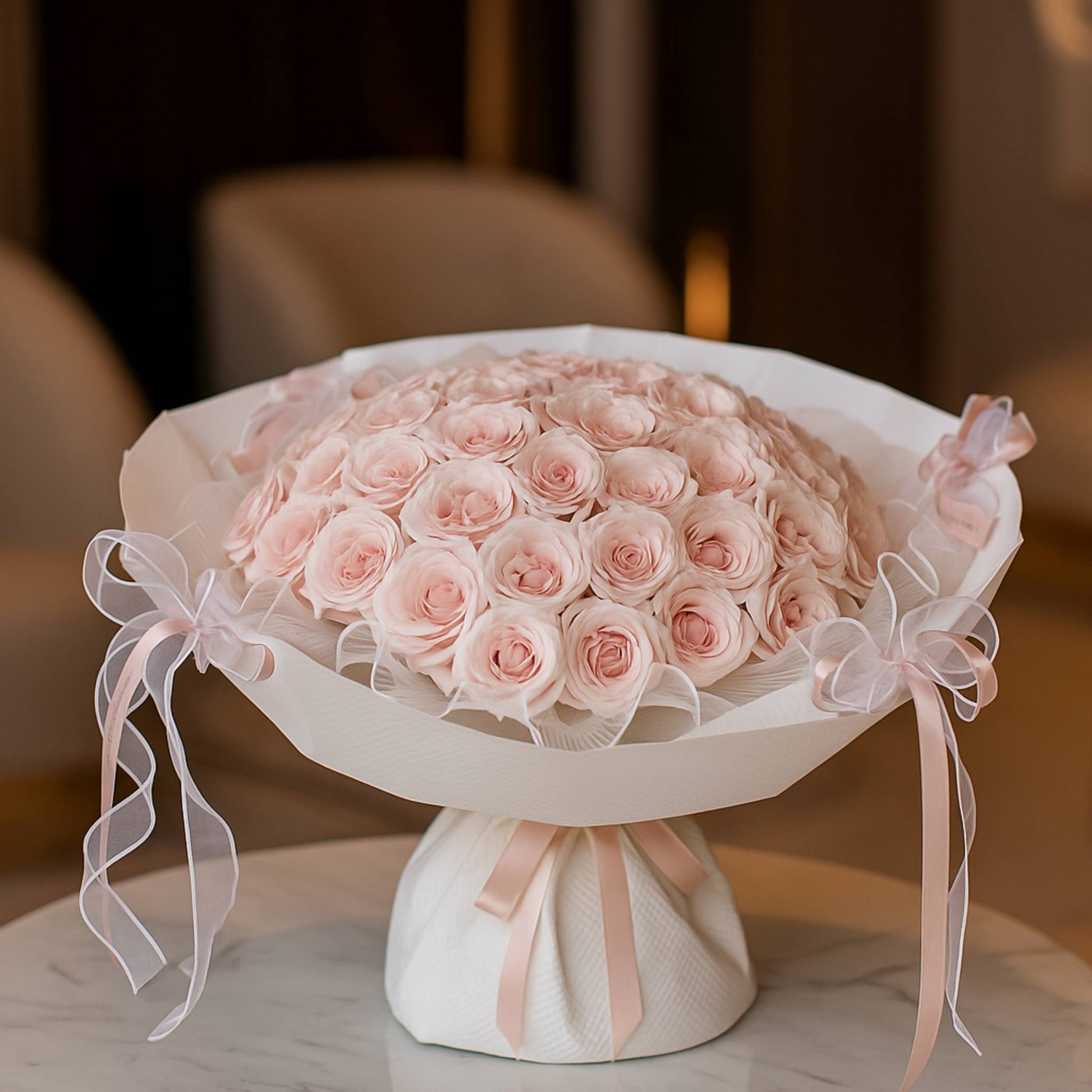 Bouquet of pink roses on a white pedestal with ribbons against a blurred background