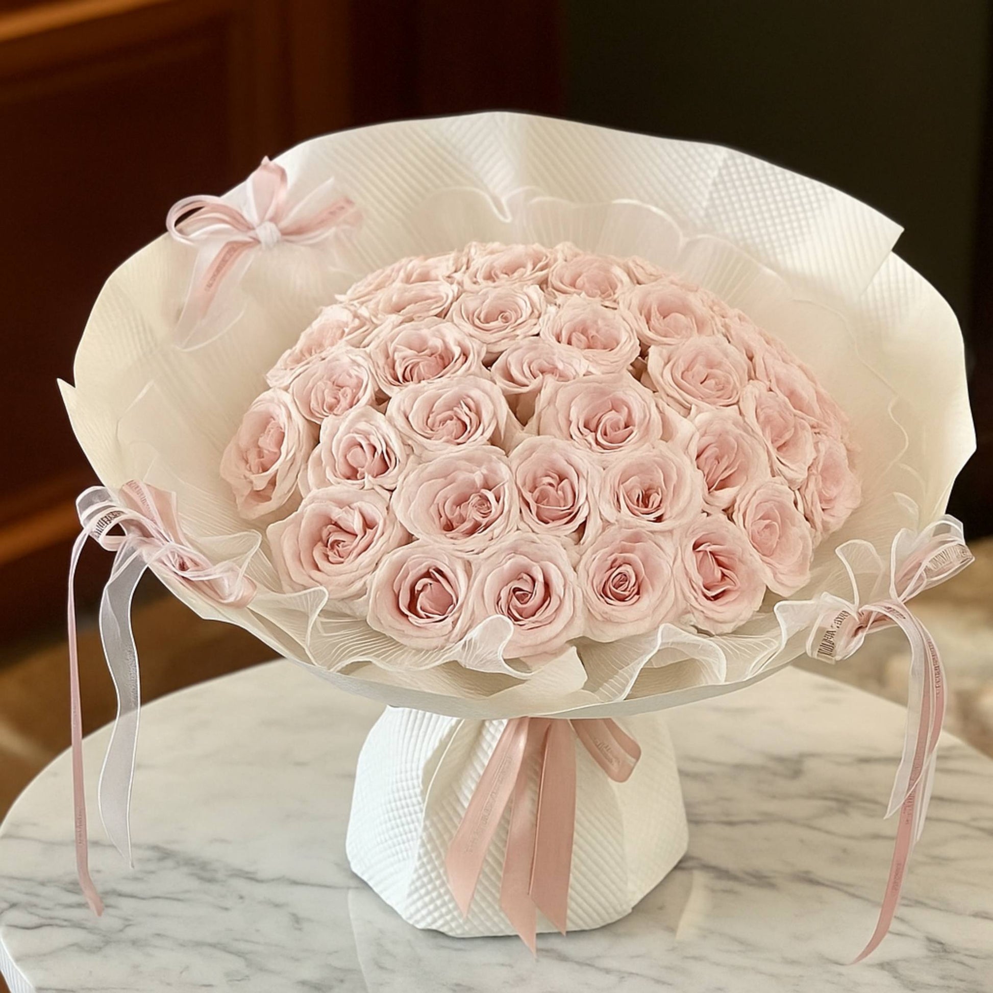 Bouquet of pink roses wrapped in white paper with a bow on a marble surface.