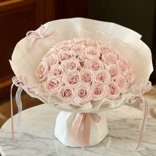 Bouquet of pink roses wrapped in white paper with a bow on a marble surface.