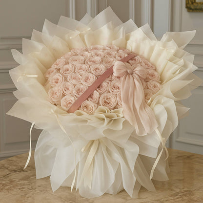 Large bouquet of pink roses with white paper and ribbons on a wooden surface.