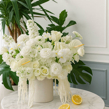 Bouquet of white flowers in a vase on a marble surface with green plants in the background.