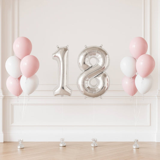 Silver '18' balloons with pink and white balloons on a light wooden floor against a white wall.