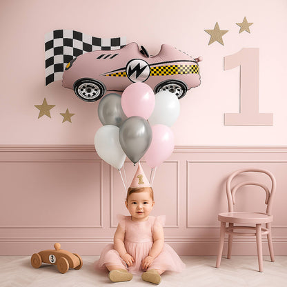 Baby celebrating a first birthday with balloons and a car-themed backdrop