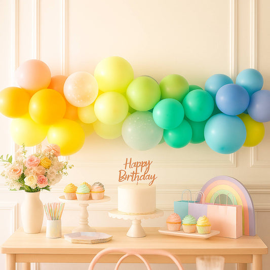 Birthday setup with rainbow balloons, cake, and decorations on a table.