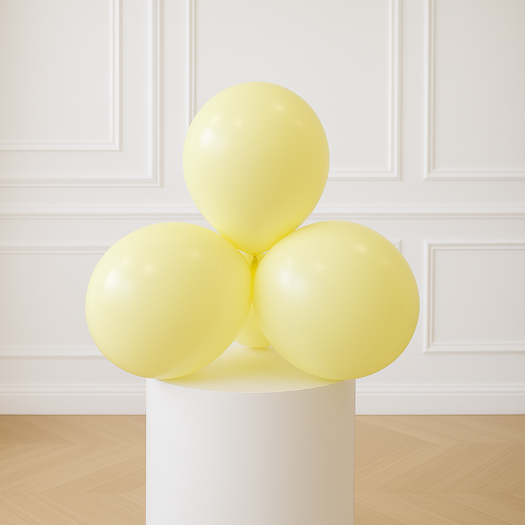Three pastel yellow balloons on a white pedestal against a white paneled wall.