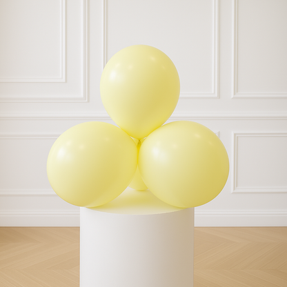Three pastel yellow balloons on a white pedestal against a white paneled wall.