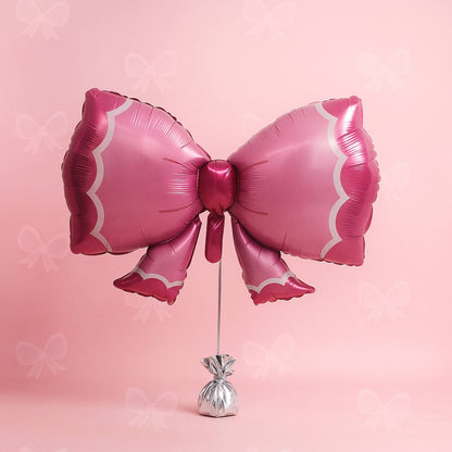 Pink bow-shaped balloon on a stand against a pink background