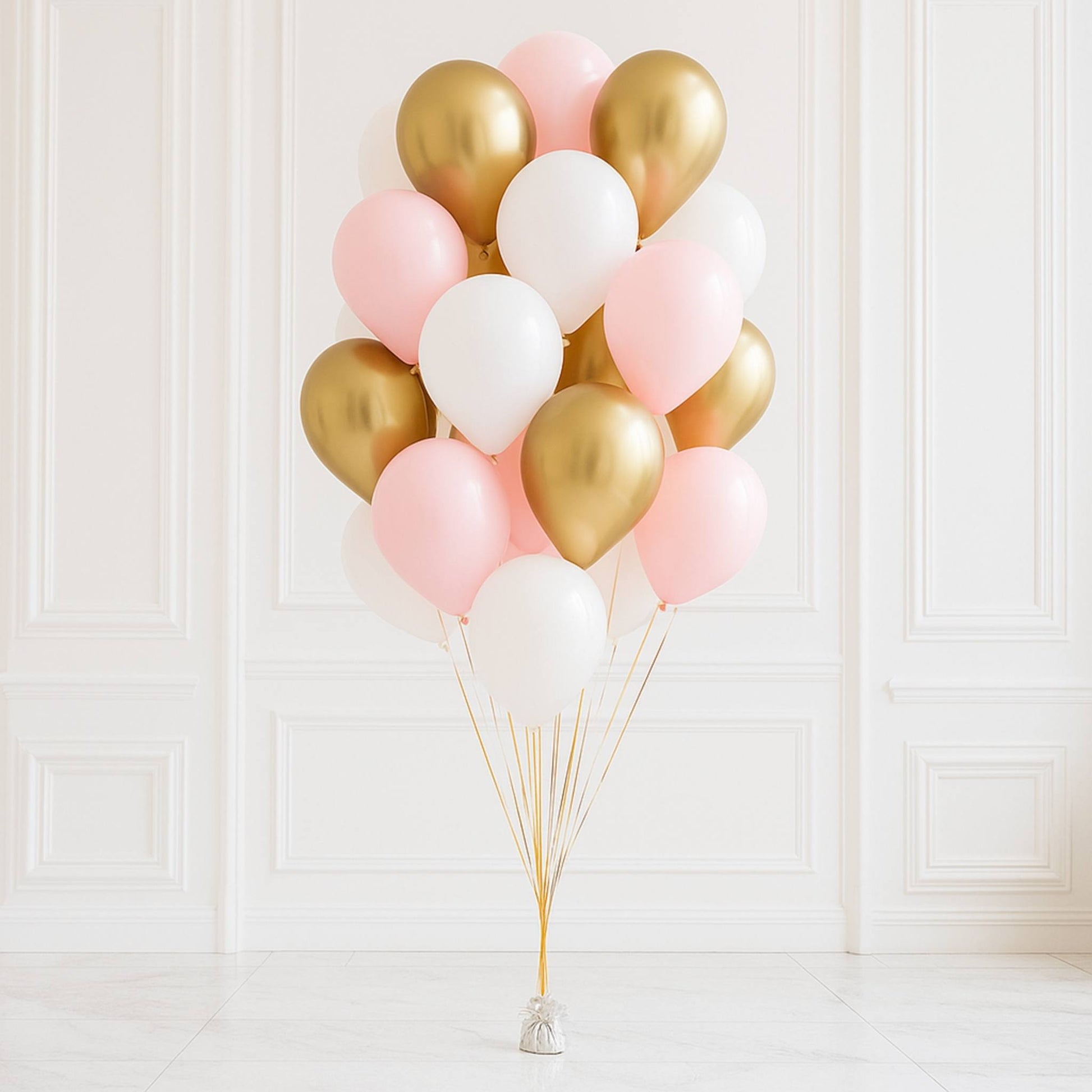 Bouquet of pink, gold, and white balloons against a white paneled wall.