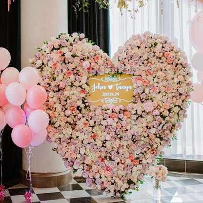 Heart-shaped flower arrangement with balloons and a personalized sign in a room.