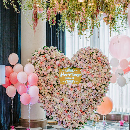 Heart-shaped floral arrangement with balloons and a decorative sign in a decorated room.
