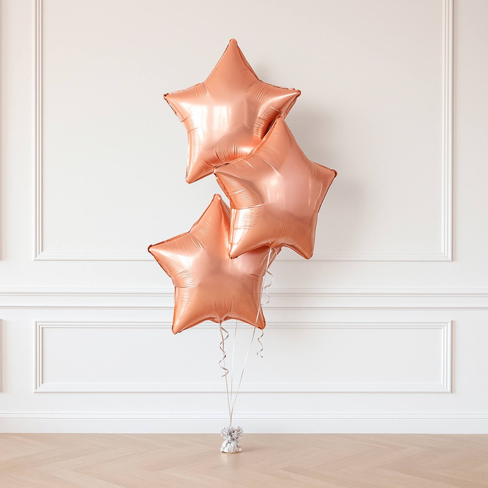 Three rose gold star-shaped balloons against a white wall.