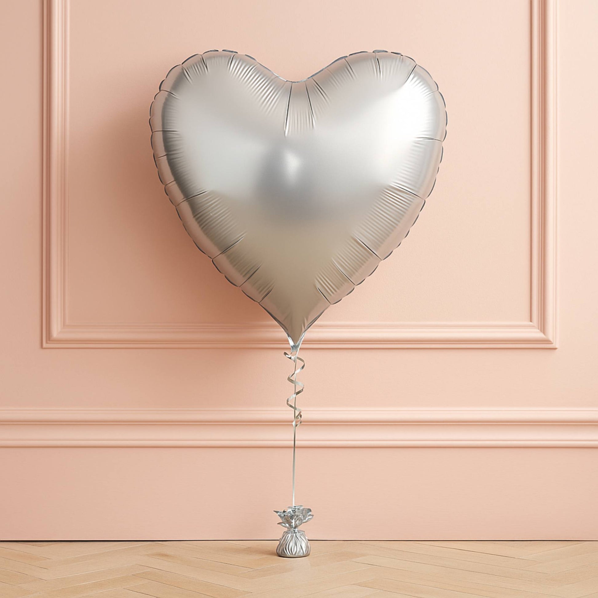 Heart-shaped silver balloon against a pink wall
