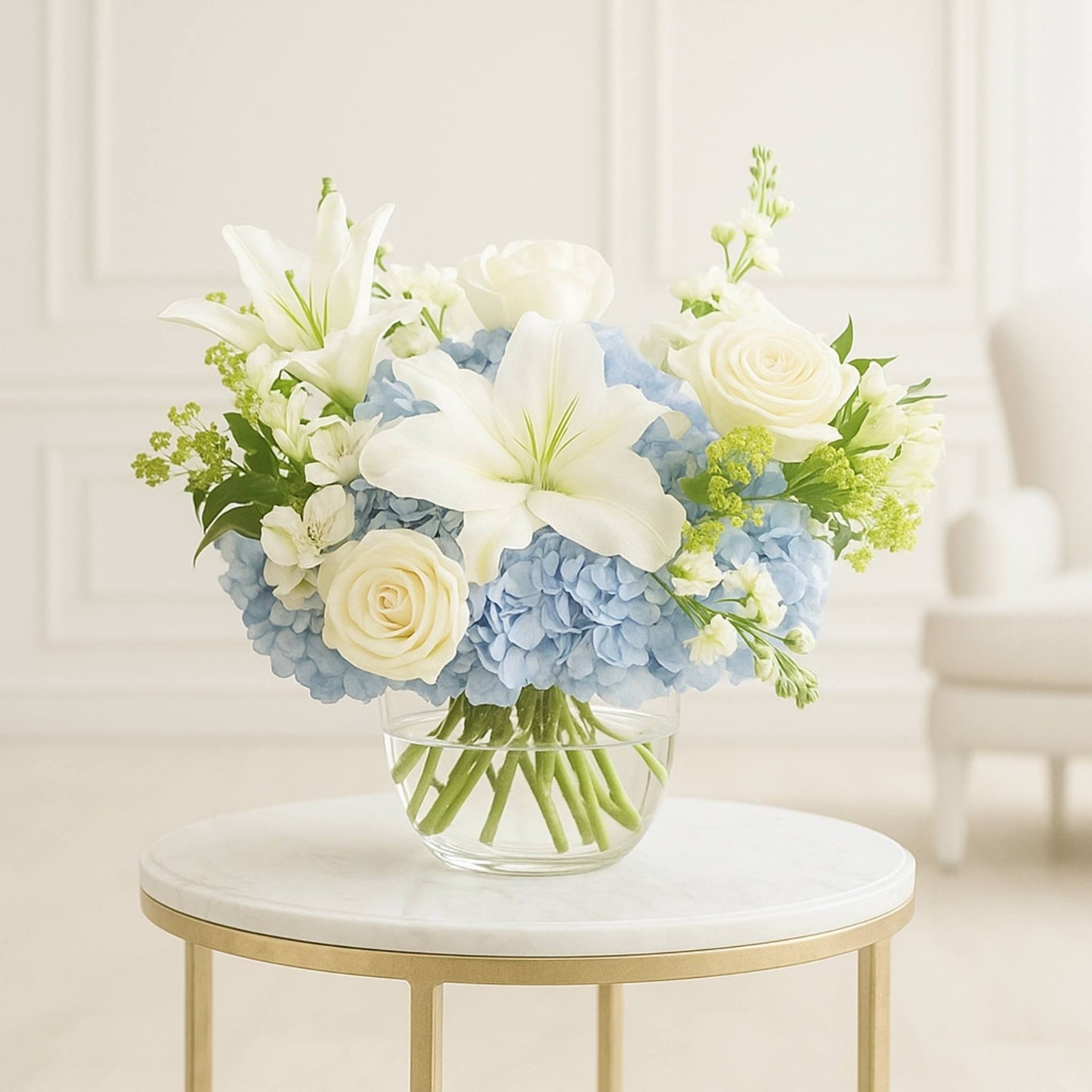 Bouquet of white and blue flowers in a clear vase on a marble table.