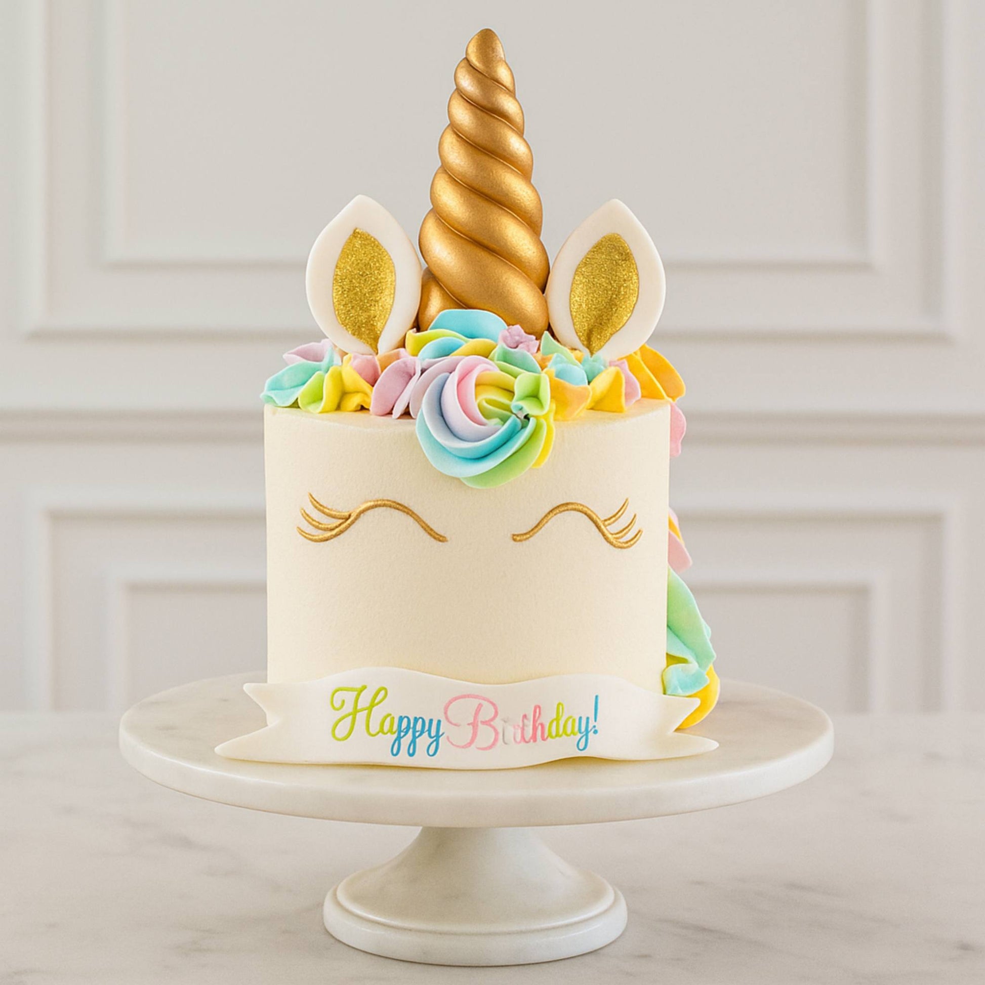Unicorn-themed birthday cake with colorful decorations on a white stand.