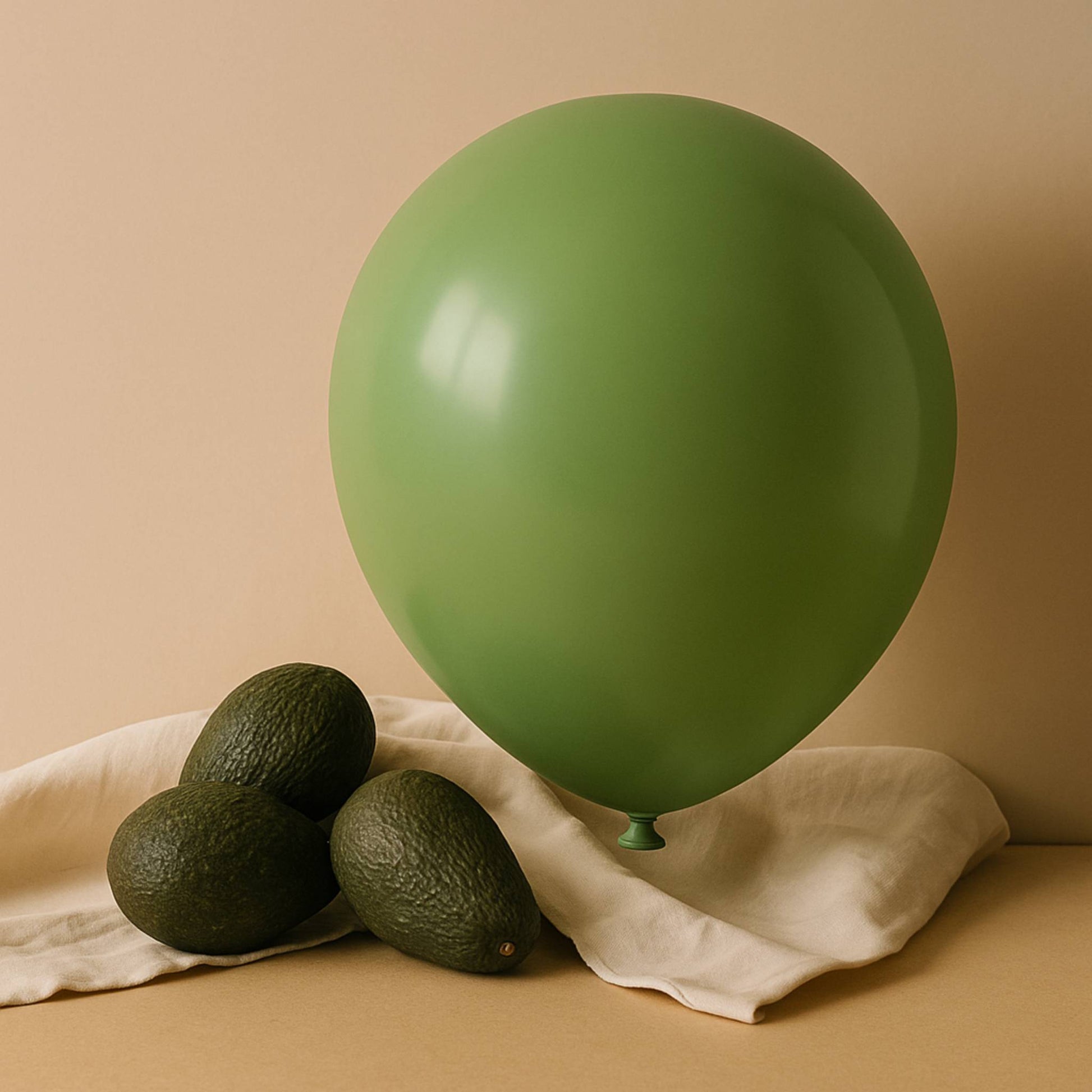 Green 11 inch helium balloon and avocados on a beige surface with a beige background