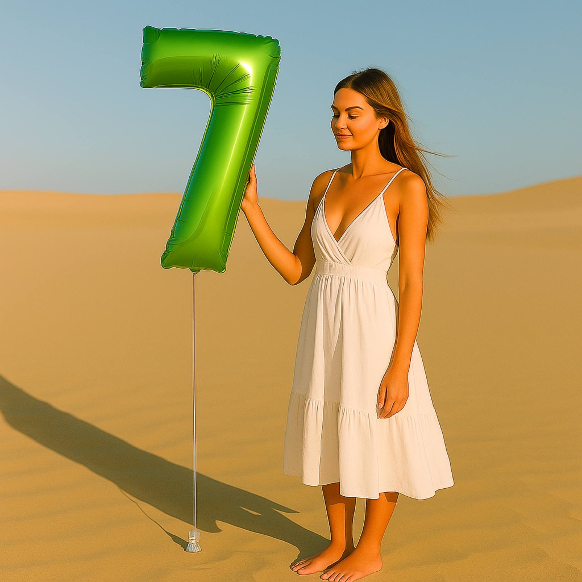 Woman in a white dress holding a large green number 7 balloon in a desert setting