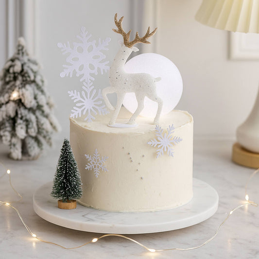White cake with deer topper and snowflakes on a marble stand with Christmas decorations.