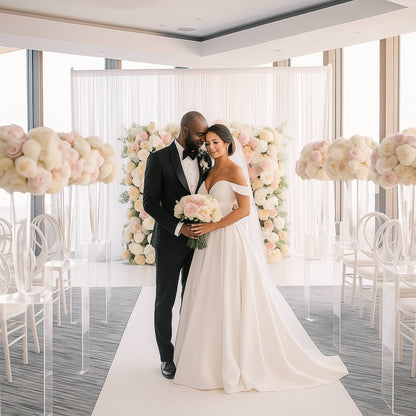 Couple in wedding attire standing in a decorated wedding hall with floral arrangements.