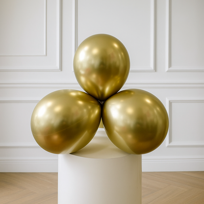 Three chrome gold balloons on a white pedestal against a white paneled wall.