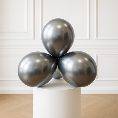 Three silver balloons on a white pedestal against a white paneled wall.