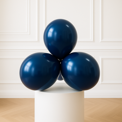 Three navy blue balloons on a white pedestal against a white paneled wall.