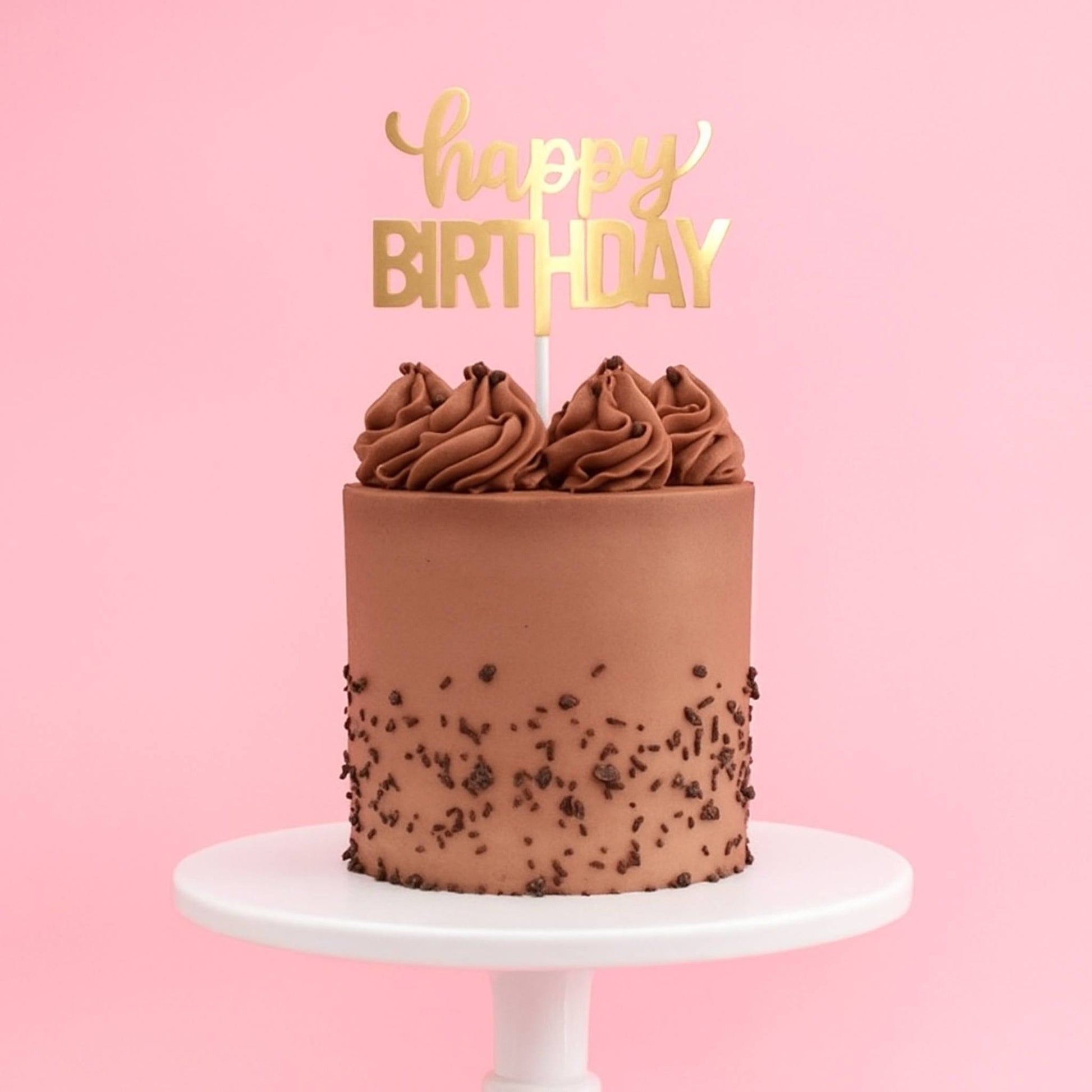 Chocolate cake with chocolate sprinkles on a white stand against a pink background