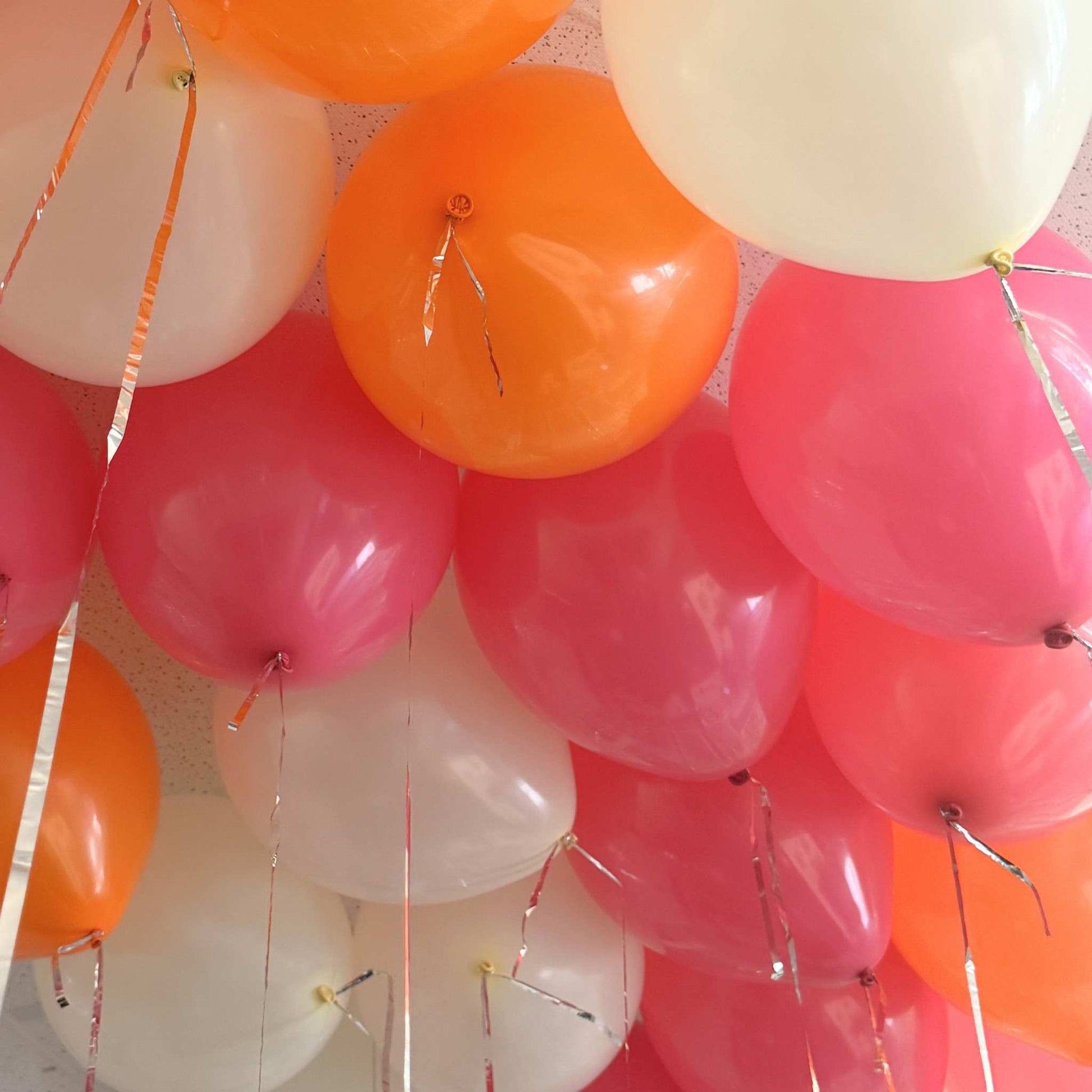 Cluster of colorful balloons in orange, pink, and white against a textured background.