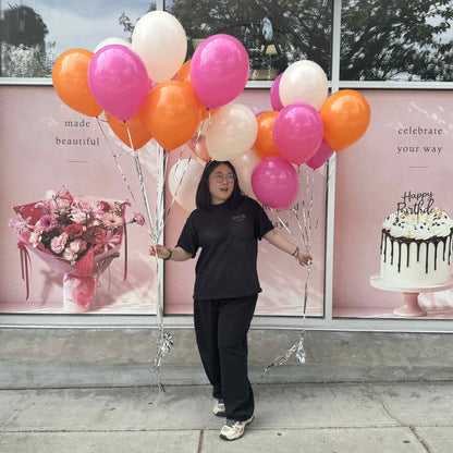 Person holding balloons in front of a store window with floral and cake decorations.