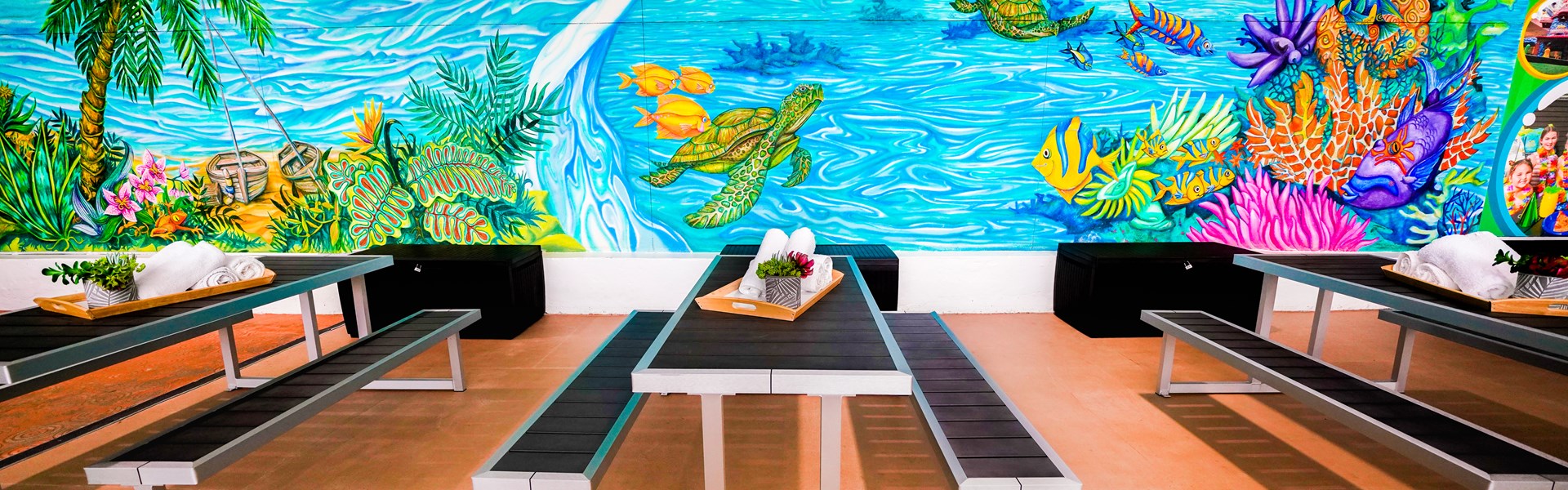 Colorful underwater-themed mural on a wall with tables and chairs in front.