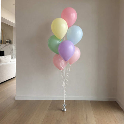 Bunch of pastel balloons tied together against a neutral wall.