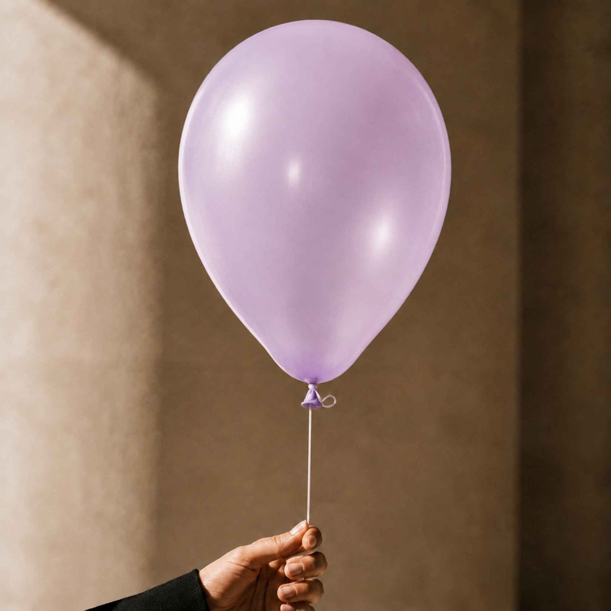 A single matte lavender balloon held by a hand against a warm beige textured background.