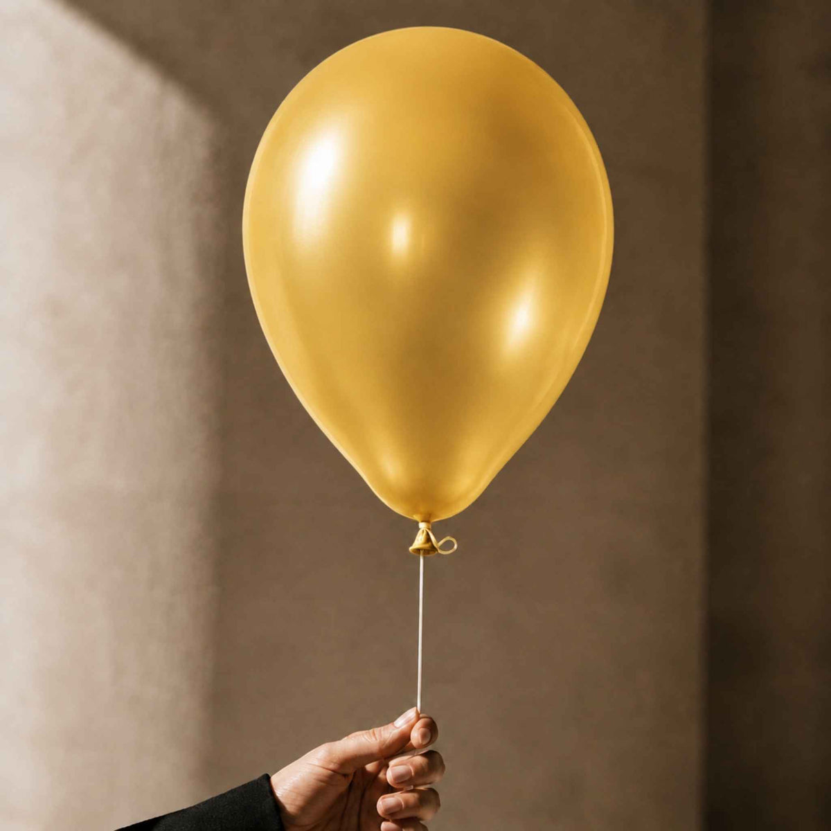 A shiny gold latex balloon held by a hand against a warm, textured brown background.