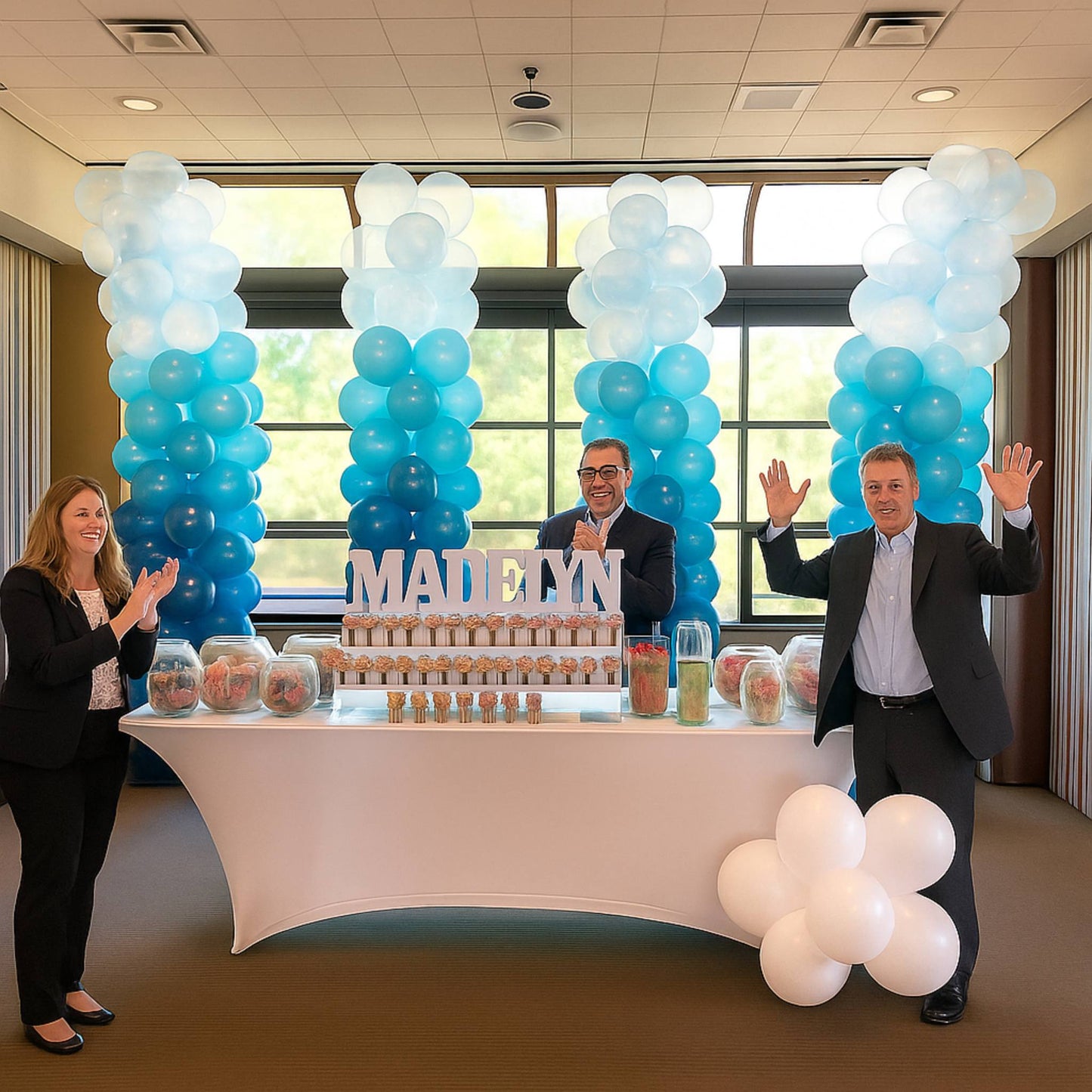 People posing in front of a table with balloons and a name display in an indoor setting.