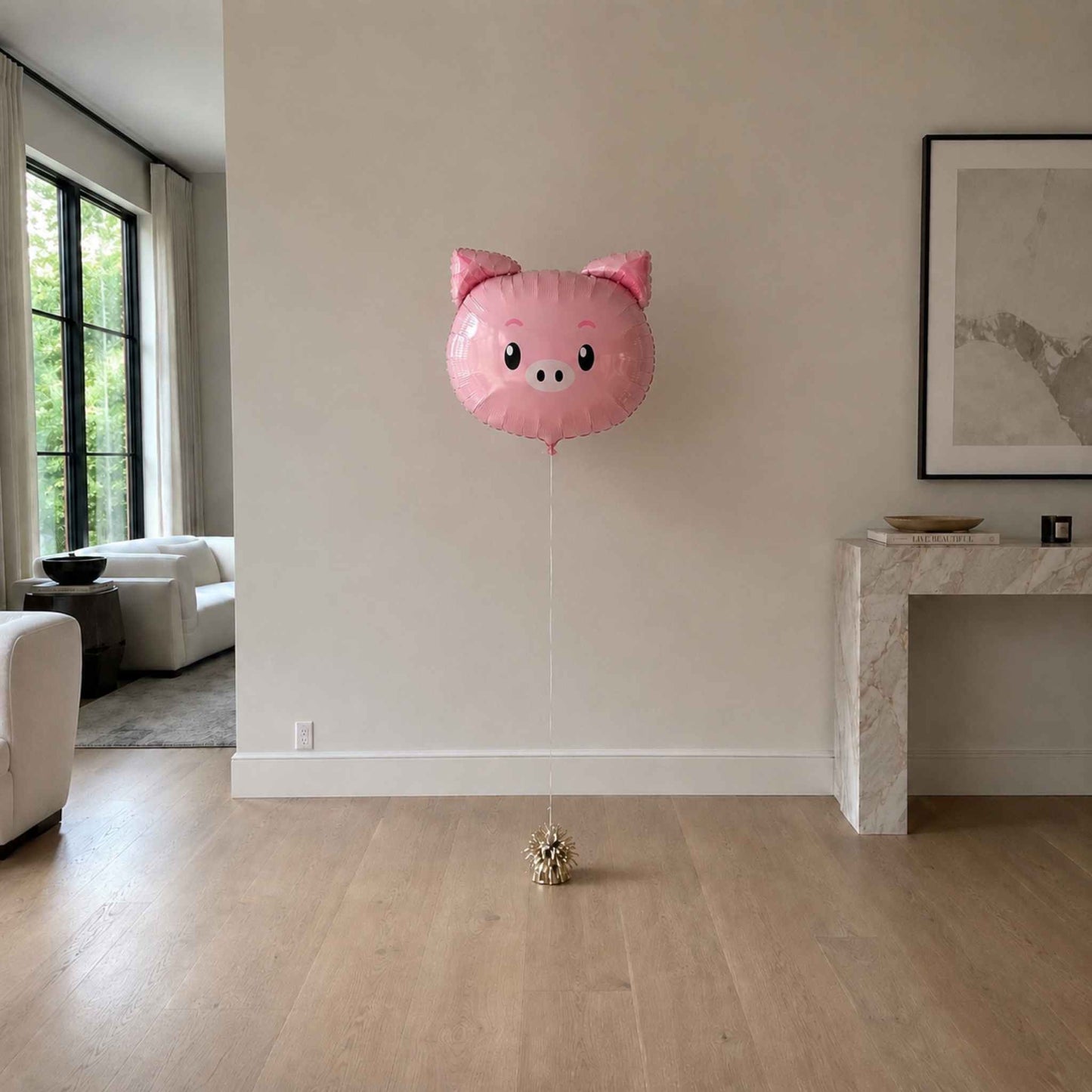 Pink pig-shaped balloon in a living room with a couch and window.