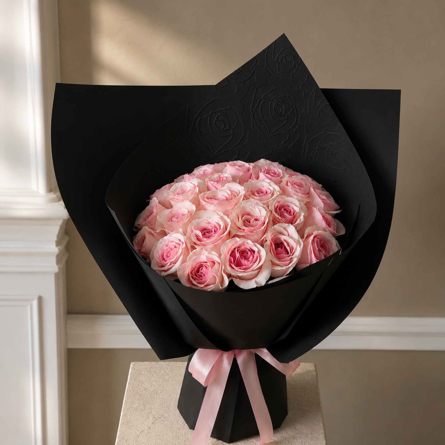 Bouquet of pink roses wrapped in black paper with a pink ribbon on a neutral background