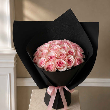 Bouquet of pink roses wrapped in black paper with a pink ribbon on a neutral background