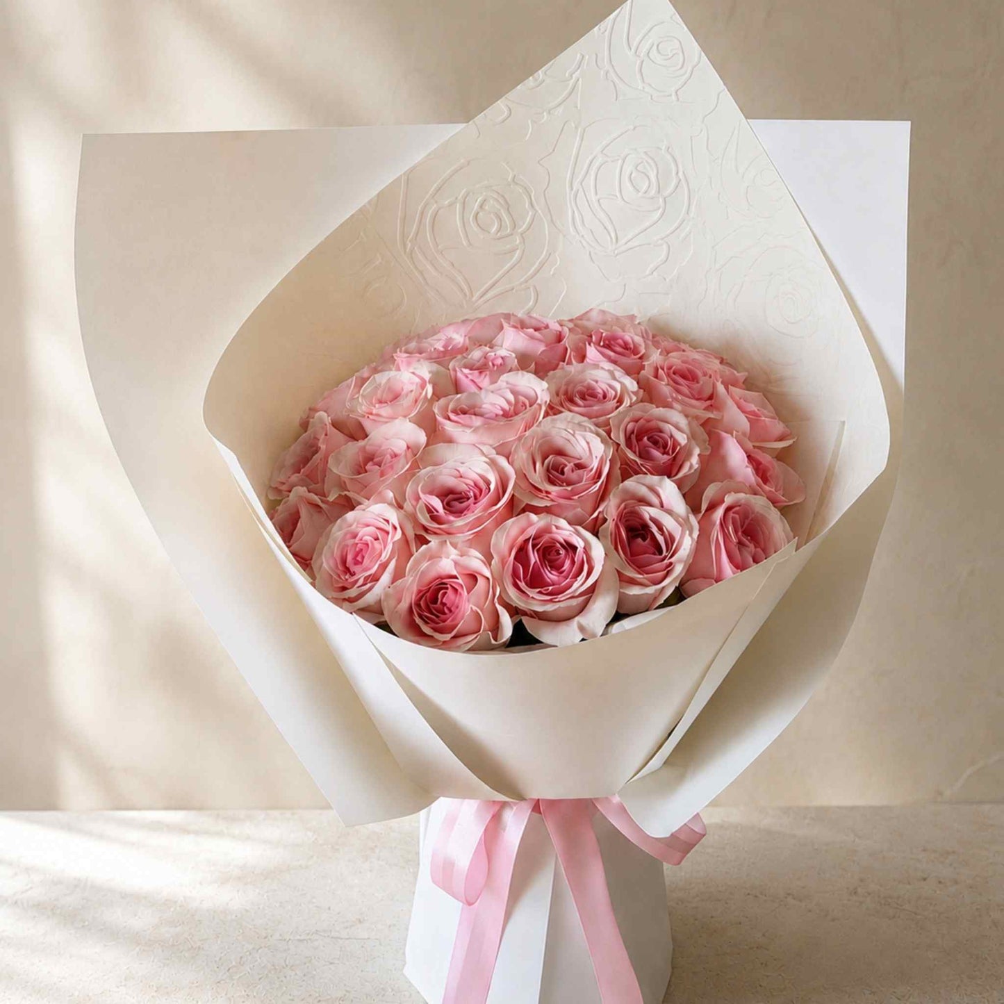 Bouquet of pink roses wrapped in white paper with a pink ribbon on a beige background