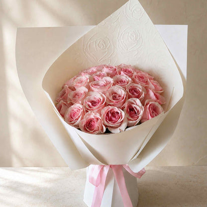 Bouquet of pink roses wrapped in white paper with a pink ribbon on a beige background