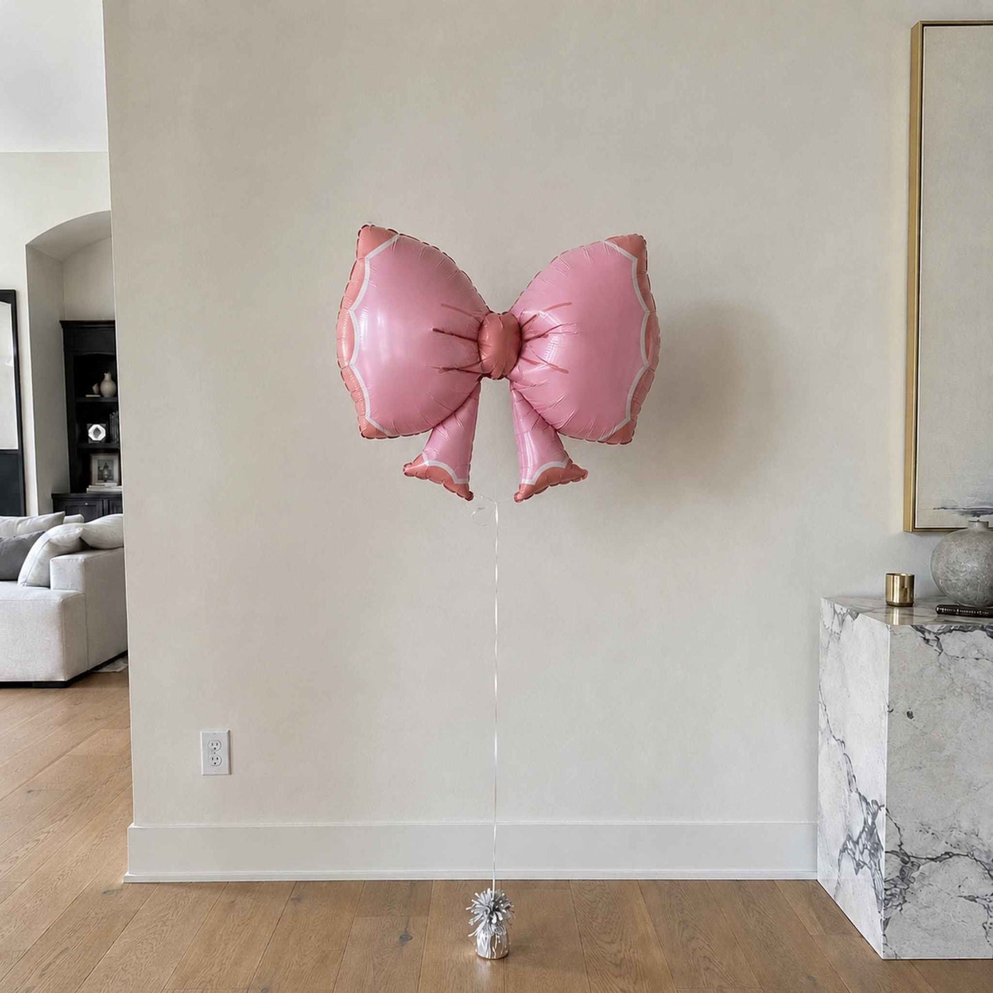 Pink butterfly-shaped balloon against a neutral wall in a room with furniture.