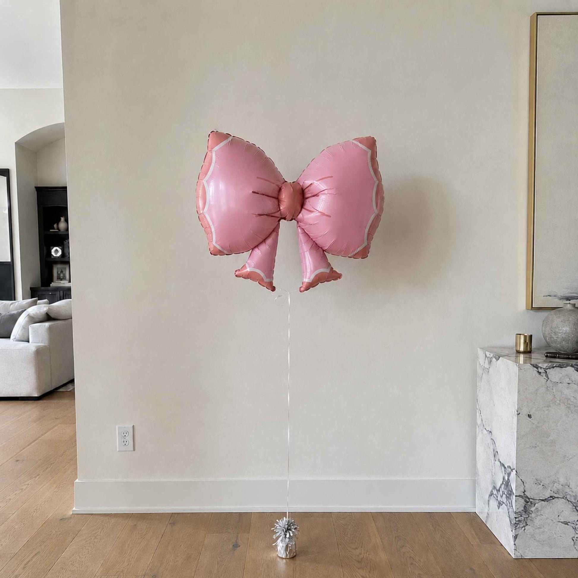 Pink butterfly-shaped balloon against a neutral wall in a room with furniture.