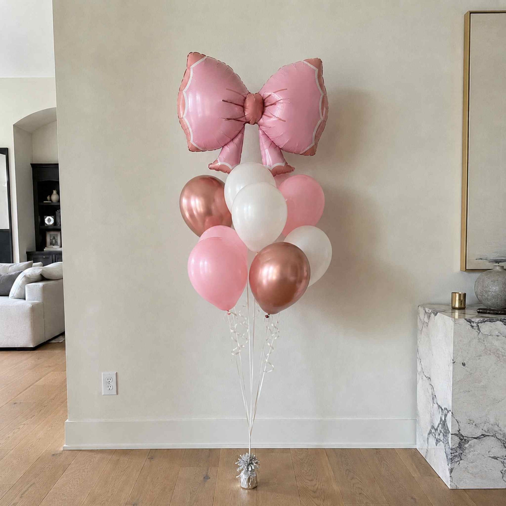 Pink and rose gold balloons with a large bow in a room setting.